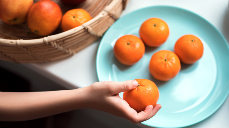 A child's hand takes a clementine off a plate