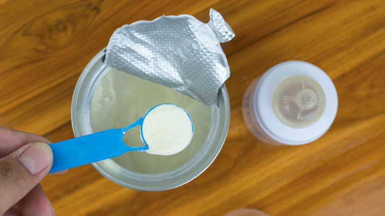 A person spooning powdered formula out of a can with a baby bottle next to the can.