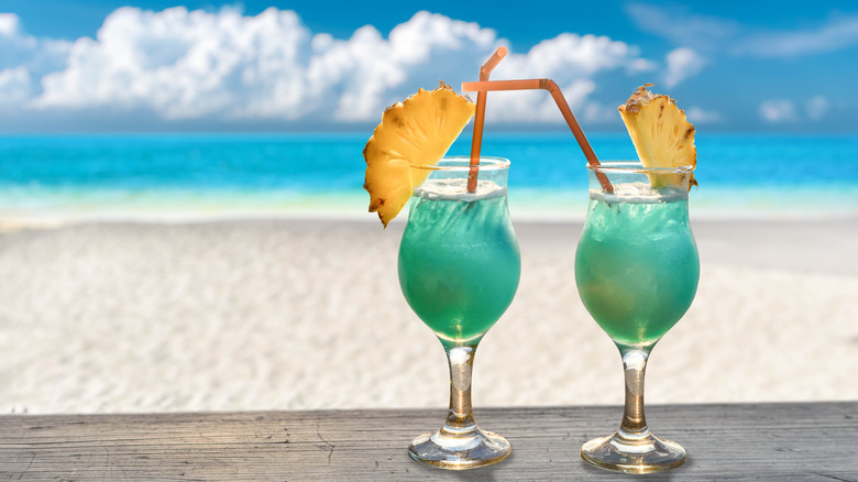 Two blue Hawaii cocktails posed on wood table with a view of the beach