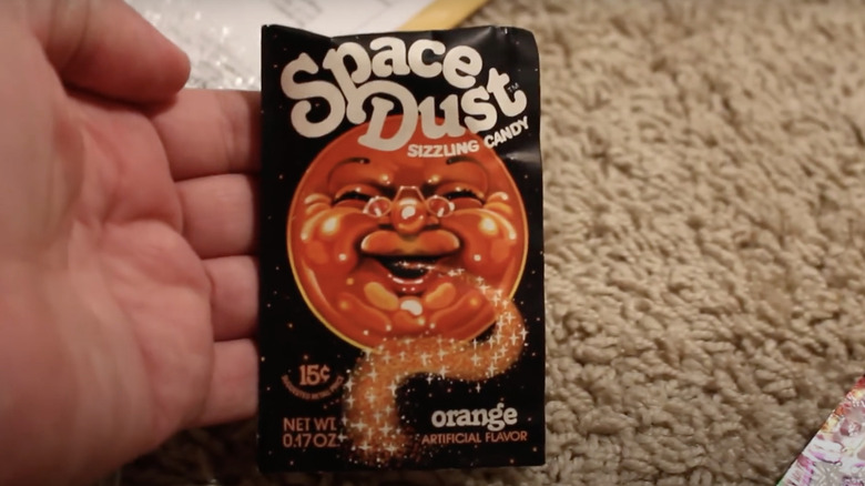 Hand holding Space Dust sizzling candy in orange flavor