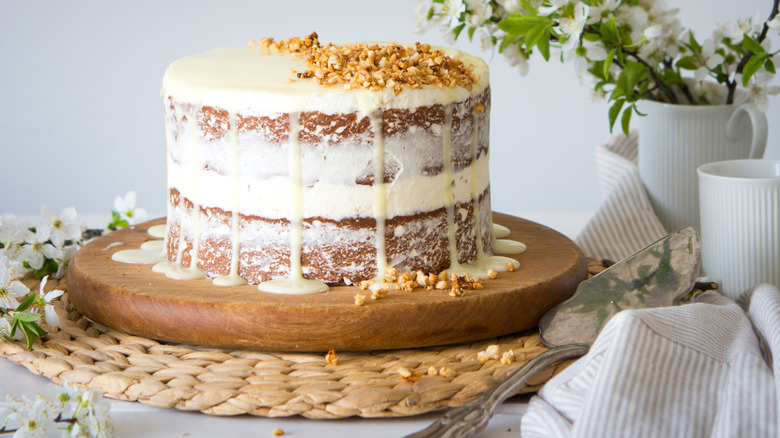 A naked cake with white frosting and chopped nuts on top
