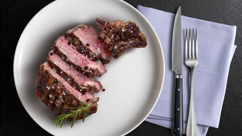 Top view of a slice ribeye steak with cutlery next to it