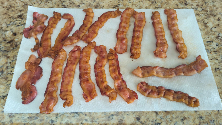cooked bacon resting on a paper towel on a kitchen counter.