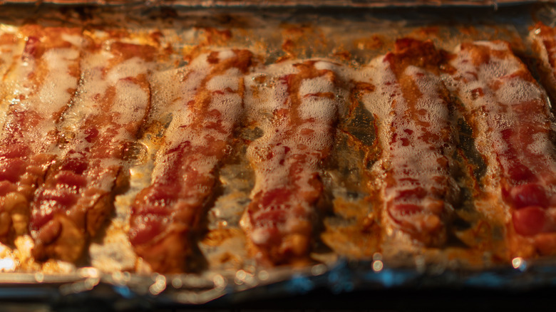 bacon sizzling in a sheet pan with grease bubbling on top of the strips.