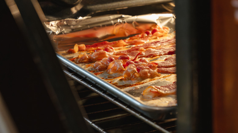 a peek into a partially opened oven while bacon cooks on a sheet pan.