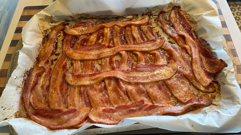 bacon shingled together in a sheet pan with three strips over the top of the initial layer.