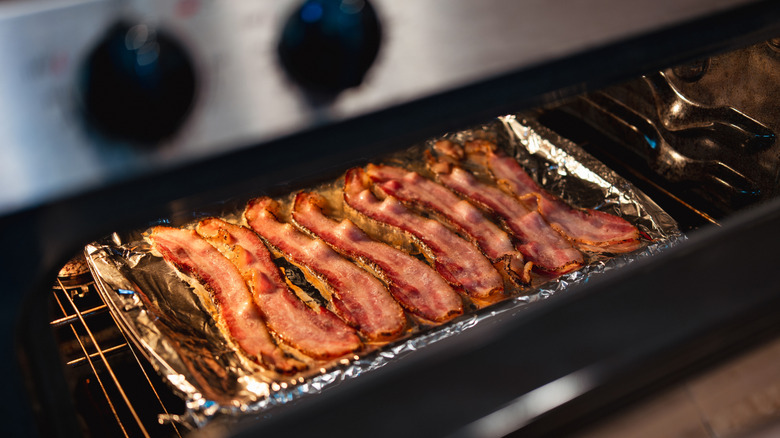 a view into an oven as strips of bacon sizzle on a sheet pan covered in foil.
