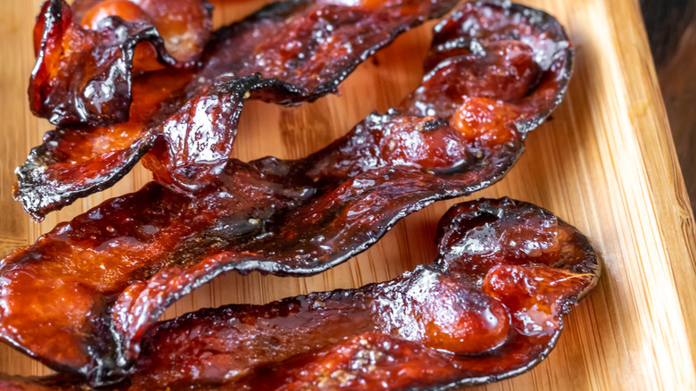 shining glaze on cooked bacon on a wooden serving tray.