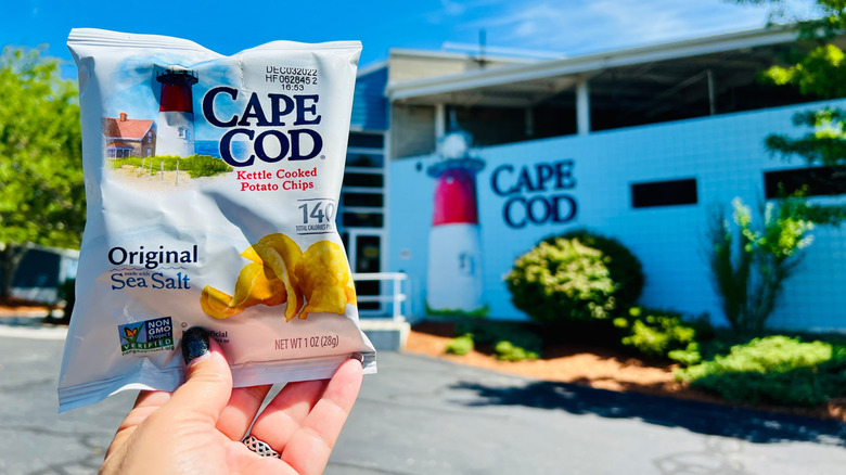 A bag of Cape Cod Original Sea Salt chips help up next to a building with the Cape Cod logo painted on the side.