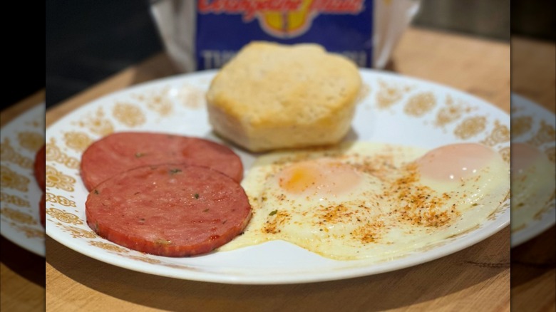 A plate of bologna, fried eggs, and a biscuit