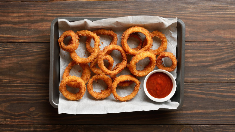 Onion rings on baking sheet with bowl of tomato ketchup