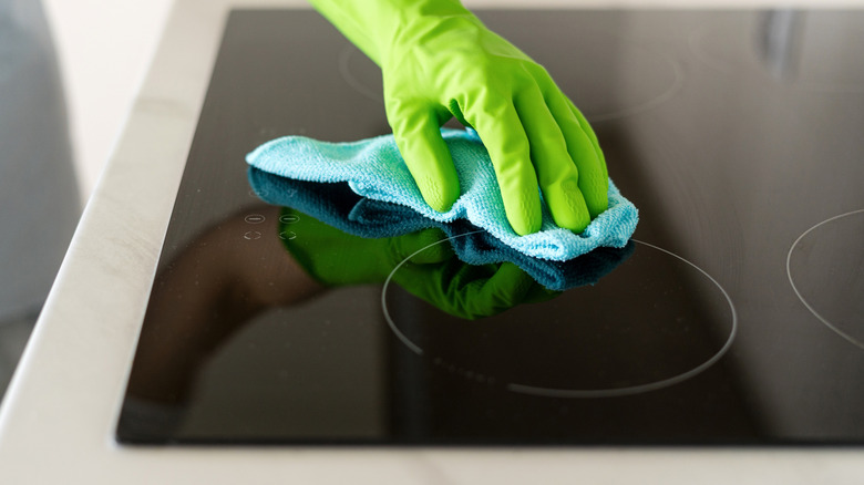 A person wearing gloves wiping a glass stovetop with a microfibre cloth