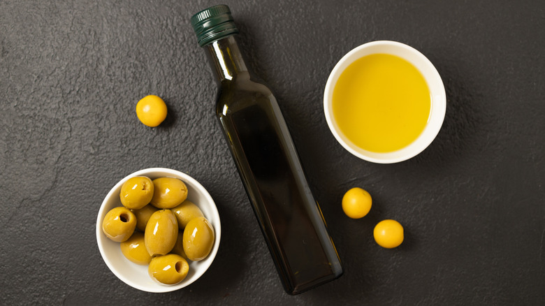 Olives and olive oil in bowls on either sides of a bottle of olive oil