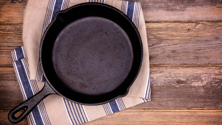 A cast iron skillet on a tea towel placed on a wooden table