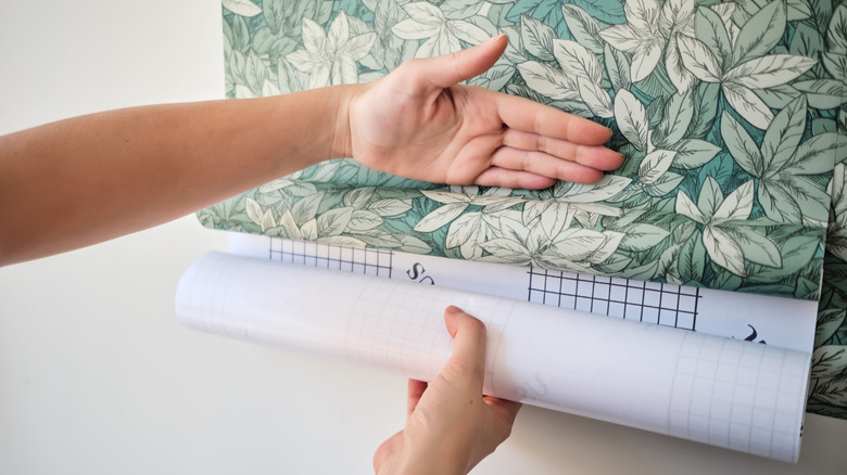 A close-up of woman's hands holding patterned contact paper to a wall