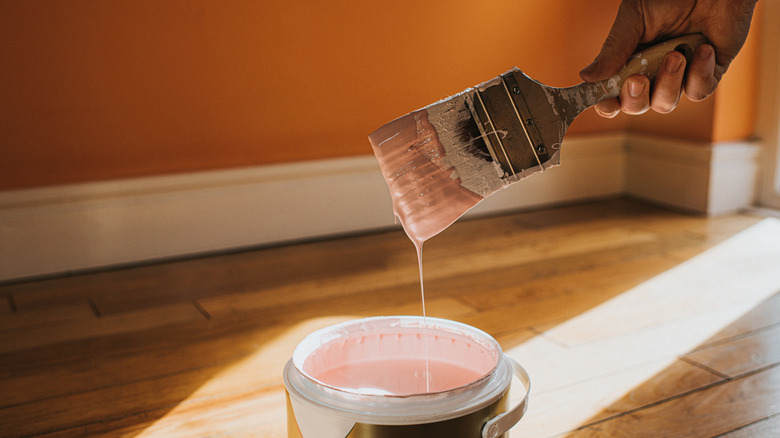 A close-up of a hand lifting a brush out of a can of paint in a home