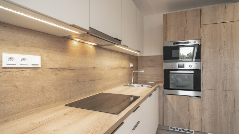 A modern kitchen with wooden backsplash, countertop, and cabinetry