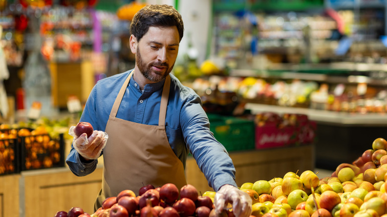 Grocery store employee arranging apples on display