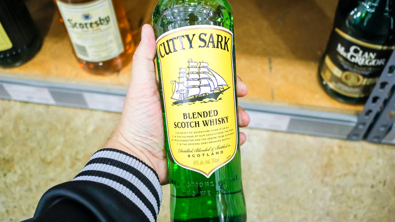 A hand holding a bottle of Cutty Sark blended scotch whisky