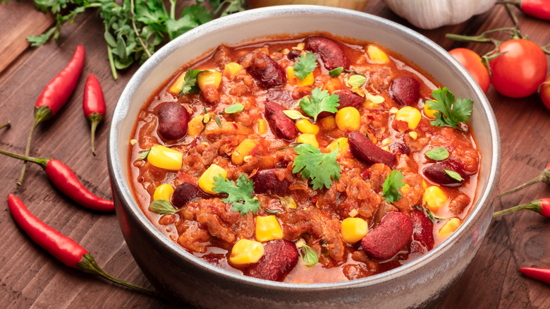 bowl of chili next to red peppers and tomatoes