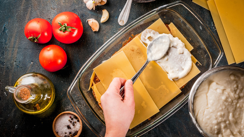 Dairy sauce being spread on lasagna