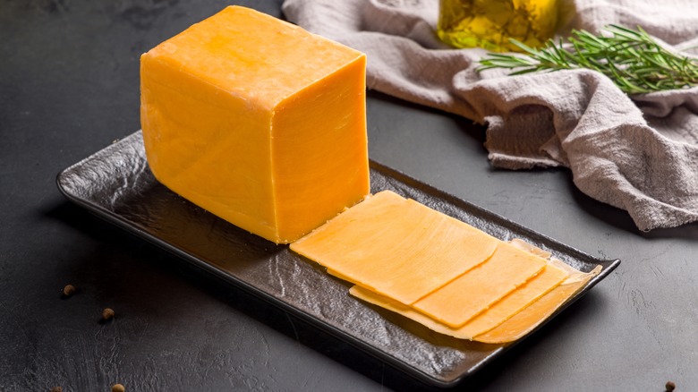 A block of orange cheddar with a few thin slices laid in front