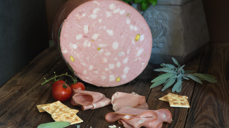 A large loaf of mortadella sliced to show marbling and pistachios inside