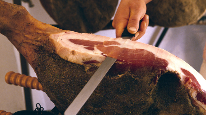 A leg of prosciutto being sliced by hand with a jamon knife