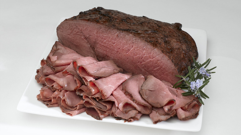 A rare cut of roast beef sliced thin for sandwiches, with an herb garnish