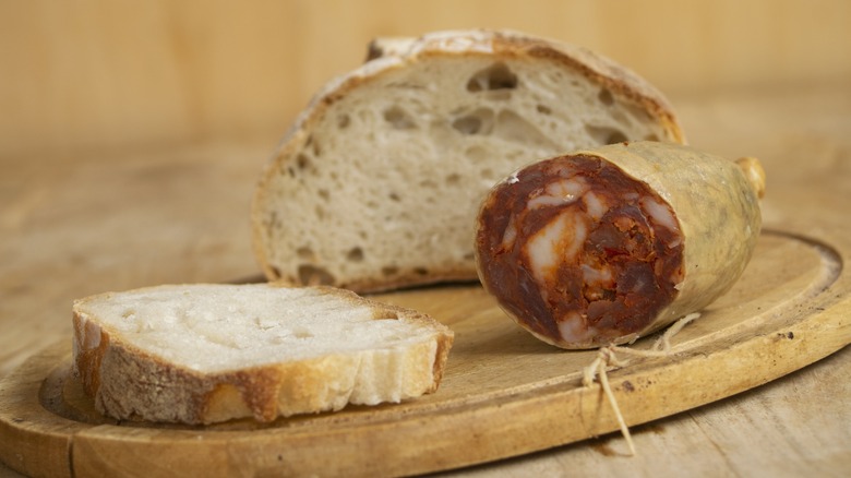 A slice of fresh bread next to an open case of sopressata salami