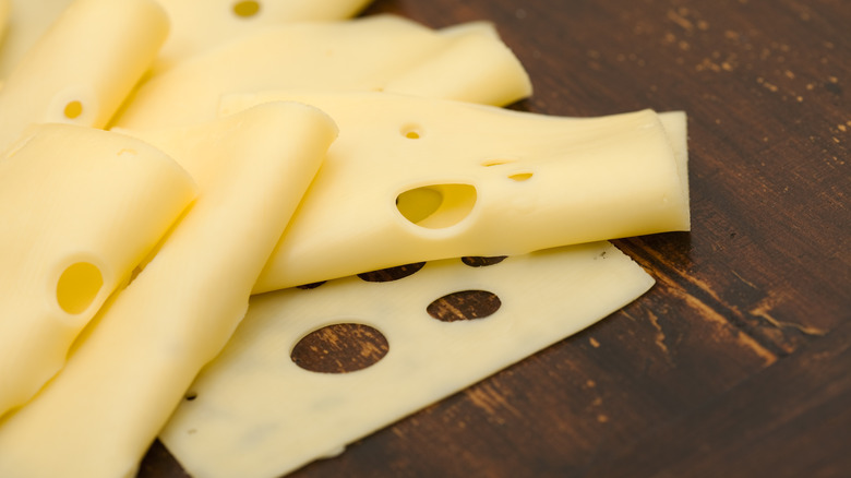 Thin slices of Swiss cheese folded on a cutting board