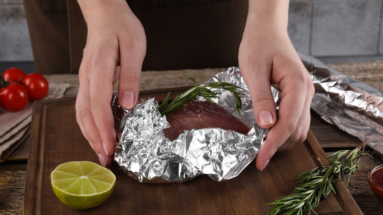 Wrapping a cut of meat in an aluminum packet with fresh rosemary