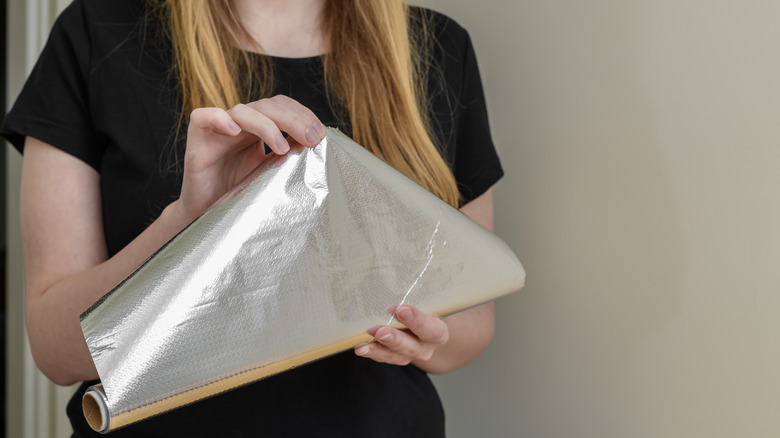 Someone unrolling a sheet of aluminum foil