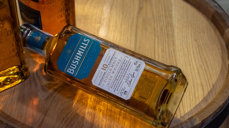 A bottle of Bushmills single malt whiskey laying on top of a wooden barrel