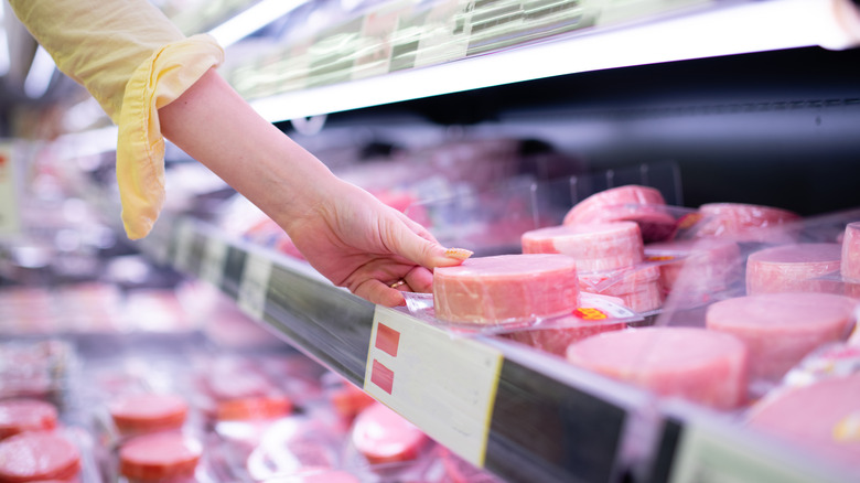 A person picking up a package of sliced ham from a grocery freezer.