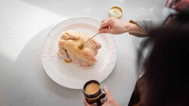 overhead shot of a woman preparing a whole chicken, on a white plate and counter
