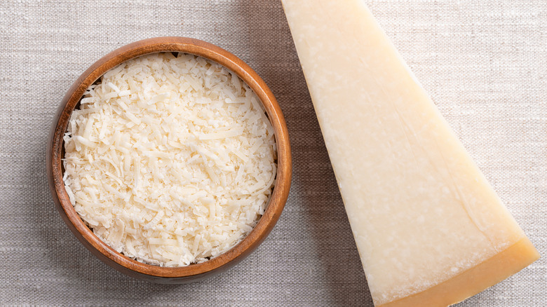 bowl of grated parmesan next to wedge of cheese against neutral background