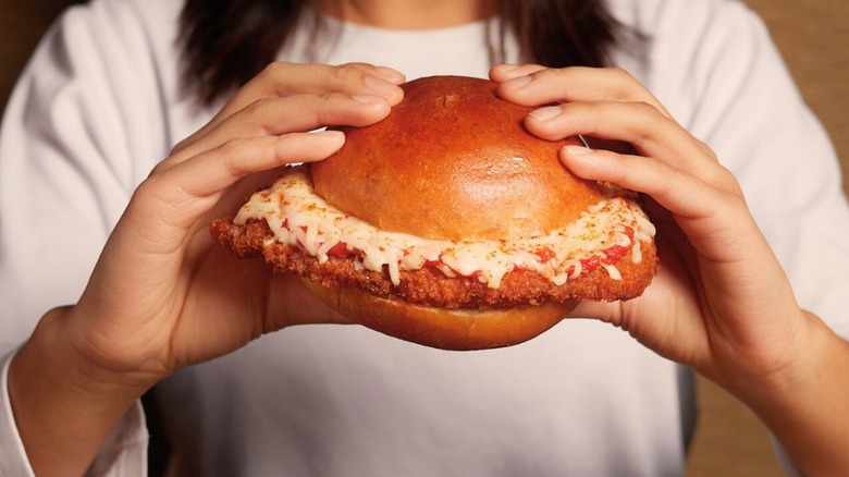 Chicken parmesan sandwich from Swiss Chalet in hands being eaten