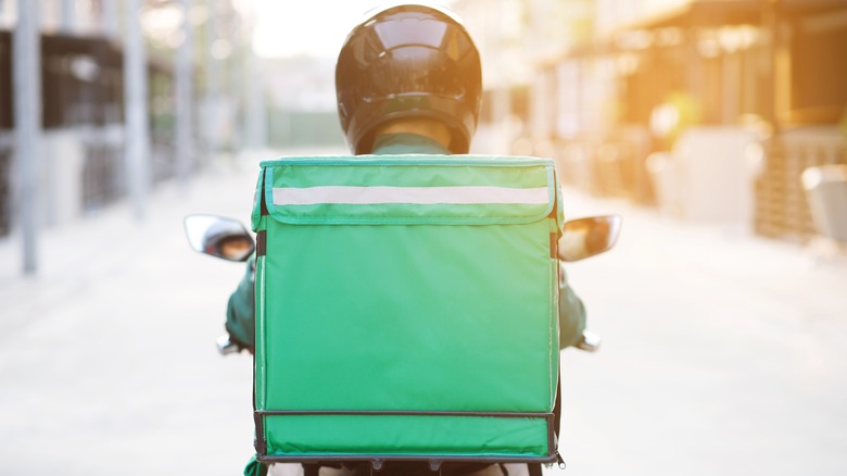 Moped delivery driver with green bag