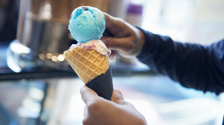 An employee topping a cone with an ice cream scoop without wearing gloves
