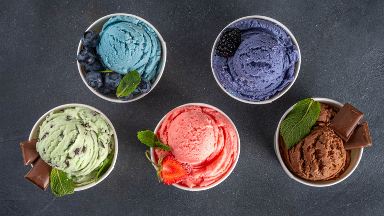 Five different flavors of ice creams in cups on a black table