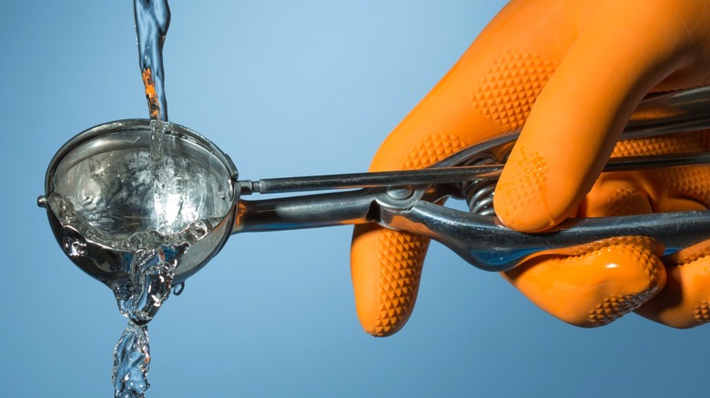 A rubber gloved hand rinsing off an ice cream scooper under water
