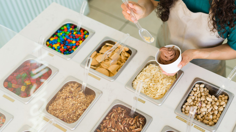 A woman adding almond flakes on ice cream from an open toppings bar