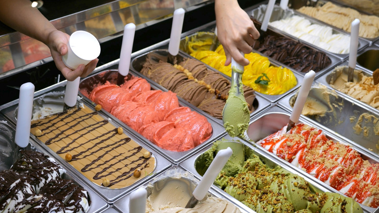 A display with different flavors of ice cream and a hand scooping some out