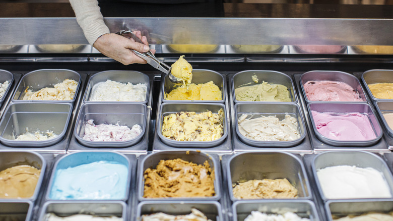 An employee scooping out ice cream from a large display with different flavors