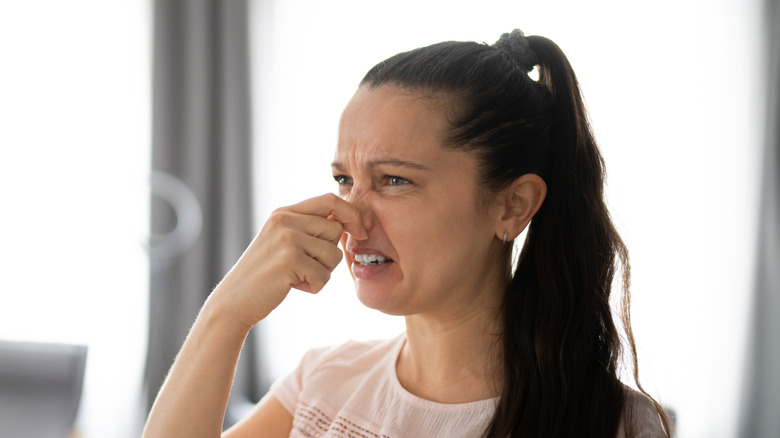A woman holding her nose due to a bad smell