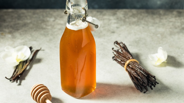 A bottle of homemade syrup with vanilla beans and a wooden honey dipper