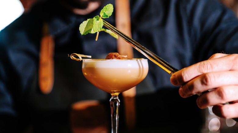 Bartender carefully adding mint leaves to a cocktail with tweezers