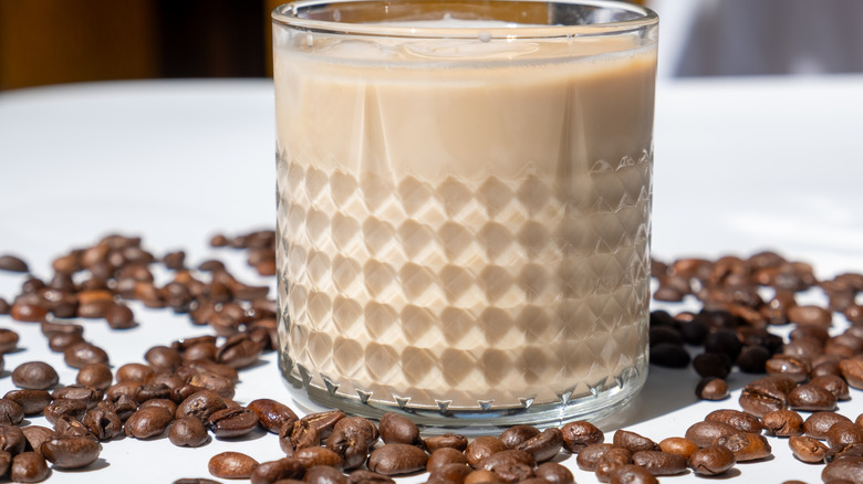 Glass of a milky coffee drink surrounded by coffee beans