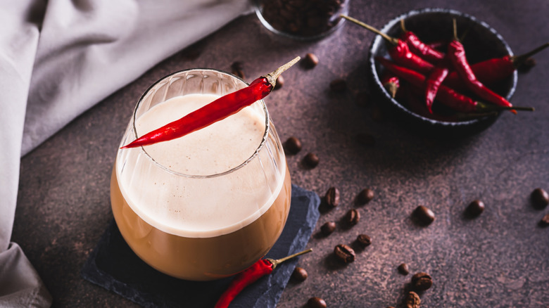 A glass of coffee cocktail and some small red chili peppers